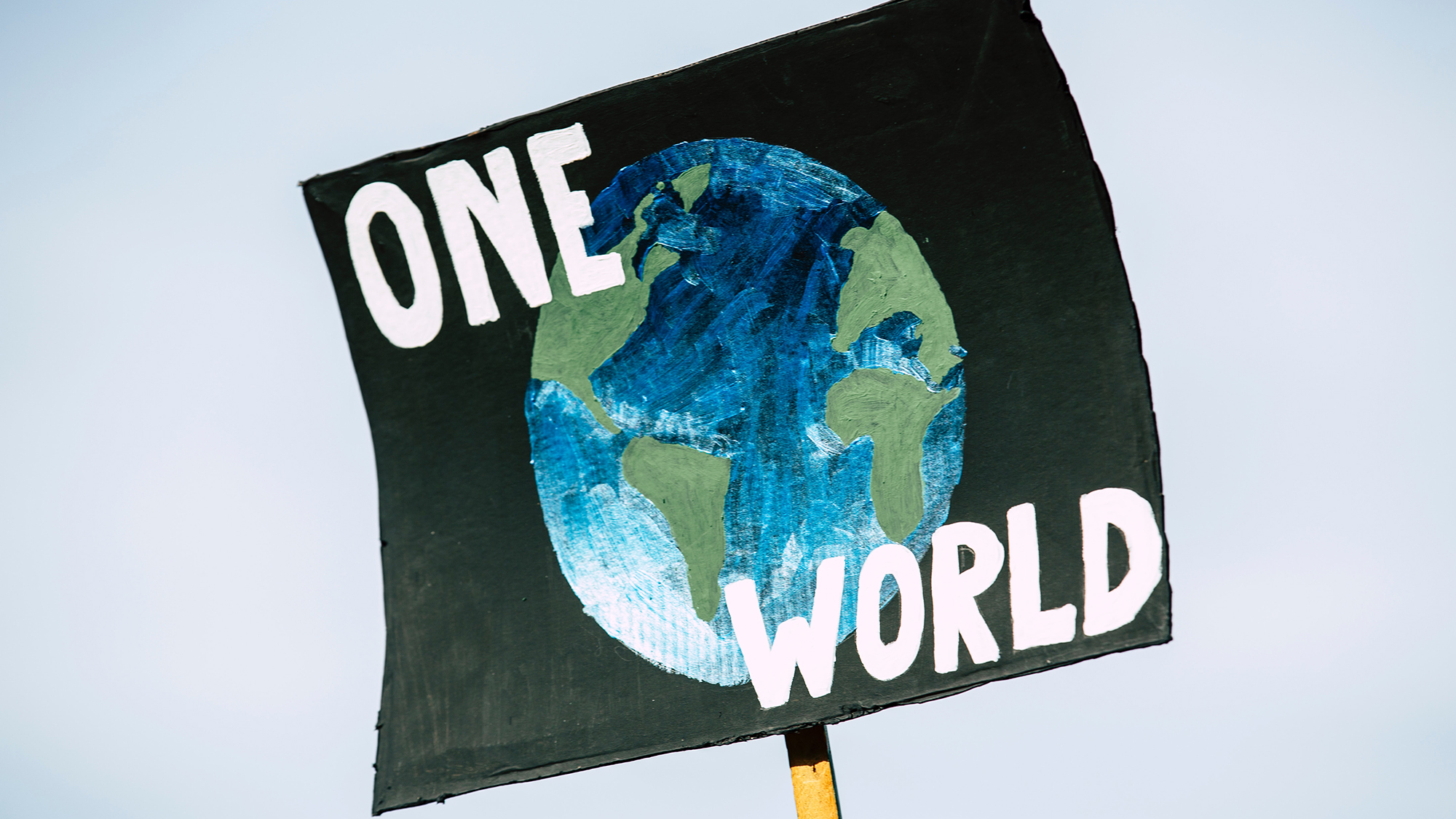 cartel pintado a mano donde se ve un globo terráqueo sobre fondo negro y unas letras blancas que dicen 'one world'.