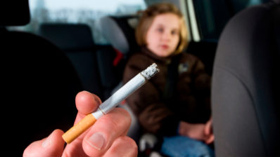 Primer plano de un cigarrillo. En el asiento de atrás, una niña desenfocada