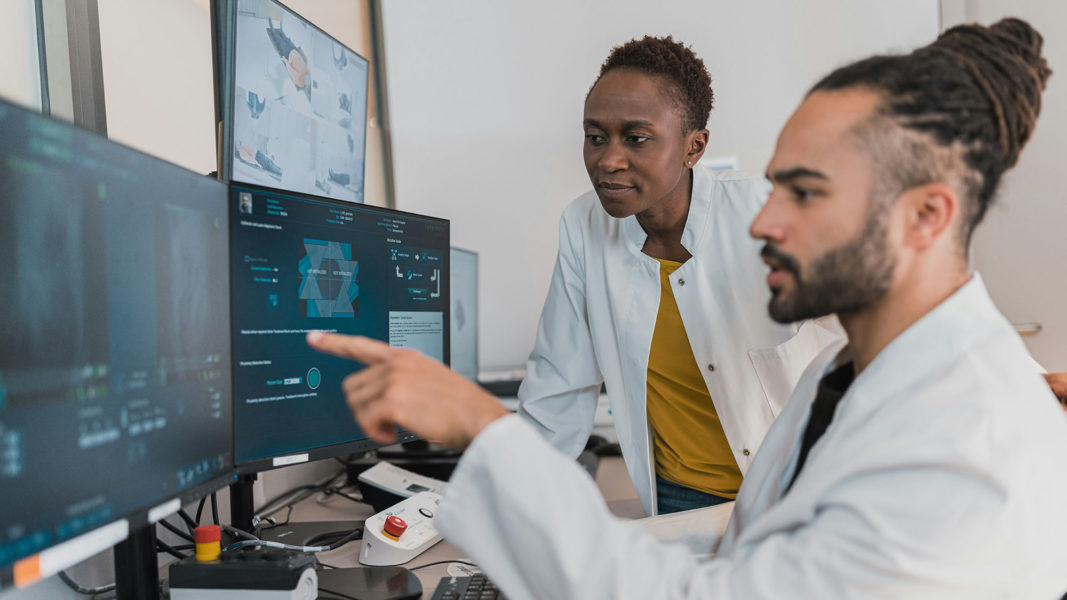 Two people in a white coat looking at a computer screen.