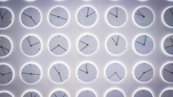 Varios relojes analógicos blancos, de distintos tamaños, dispuestos sobre una pared blanca.