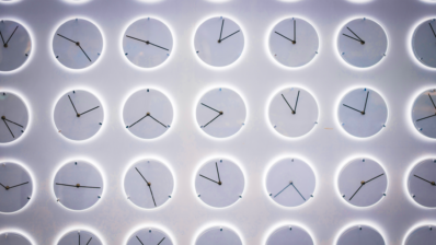 Several white analogue clocks of different sizes arranged on a white wall.