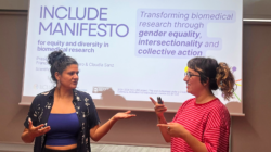 Francisca Casas-Cordero and Claudia Sanz talking in front of a screen presenting the INCLUDE Manifesto on equity and diversity in biomedical research.