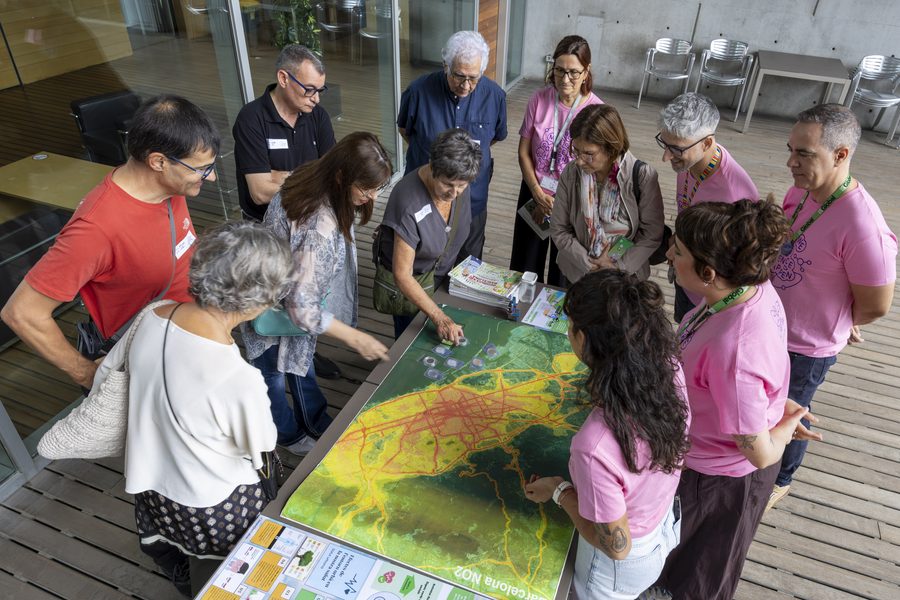 Un grup de visitants i voluntaris de l'OpenPRBB 2026 observa un mapa de Barcelona amb informació ambiental durant una activitat divulgativa.
