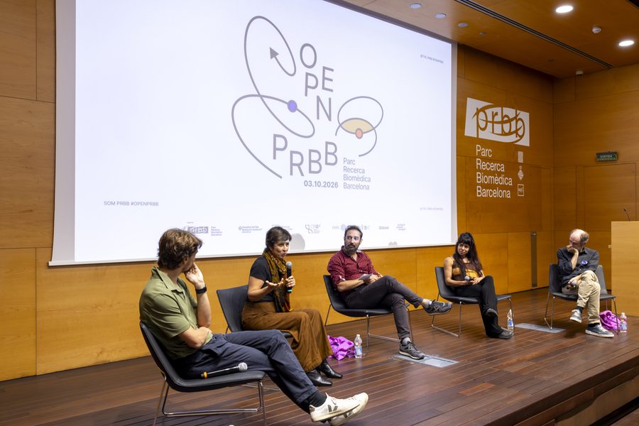 Cinc participants asseguts a l'escenari de l'auditori del PRBB durant el vermut científic de l'OpenPRBB 2026, amb el logotip de la jornada projectat al fons.