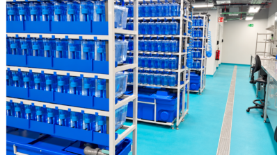 Rows of transparent tanks with blue fittings arranged on racks beside a working area in the upgraded PRBB MARS aquatic facility.